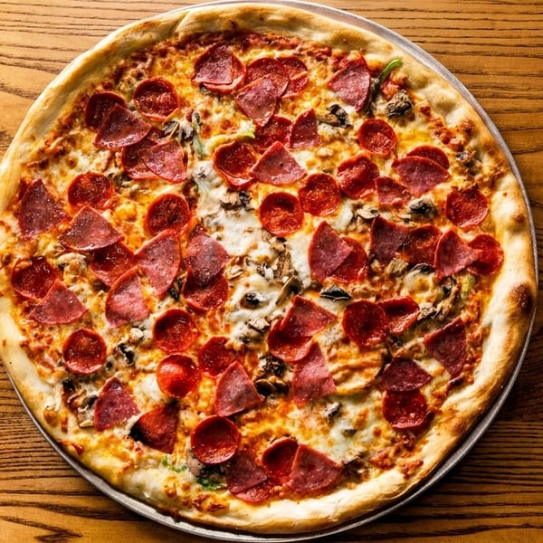A whole pepperoni, salami, and mushroom pizza on a metal pan, centered on a wooden table.