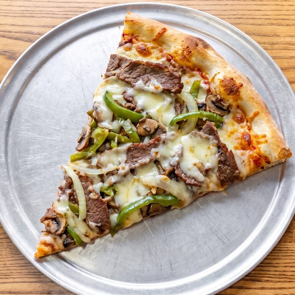 A large slice of steak and cheese pizza with green peppers, onions, and mushrooms on a metal tray.