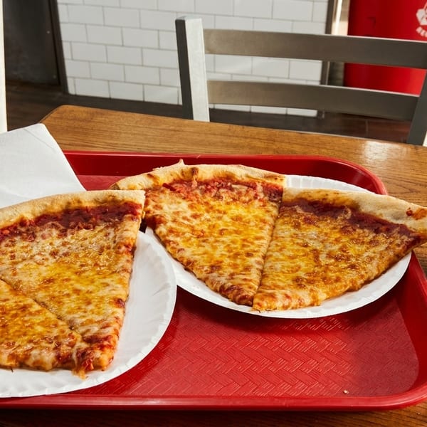 Three slices of cheese pizza on paper plates with a soda can on a red tray.